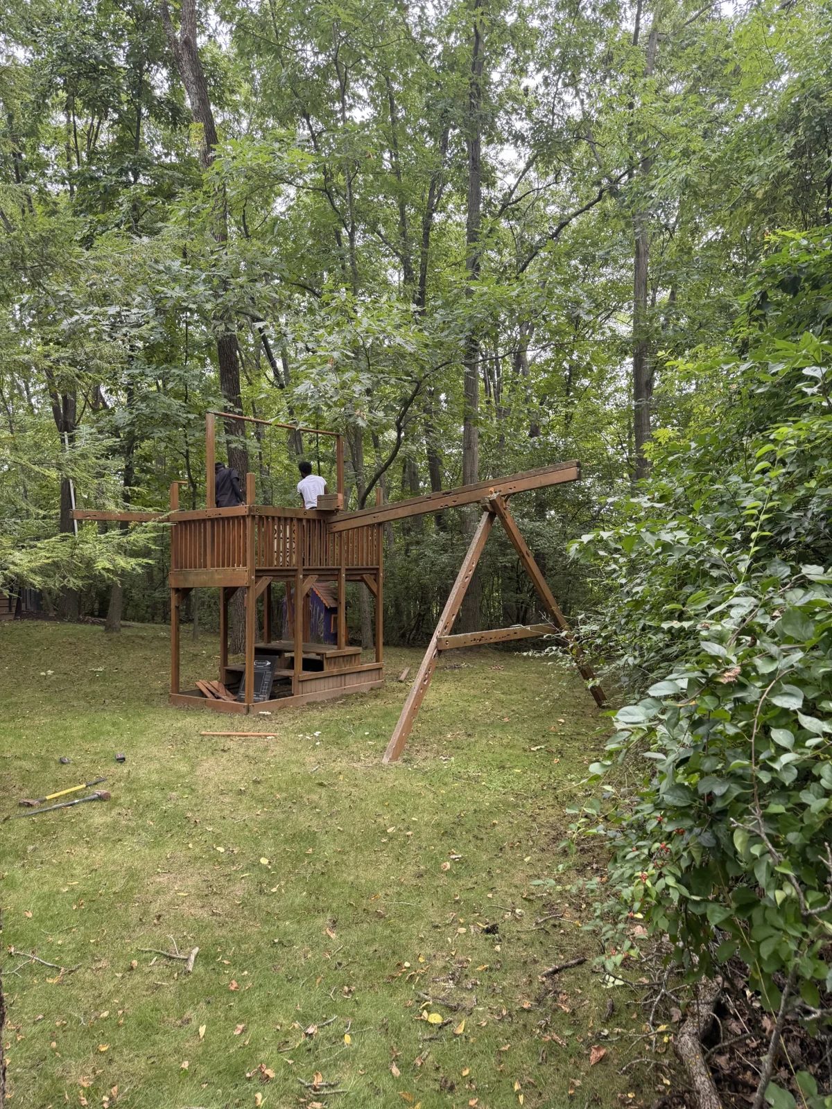 Junk Warriors crew dismantling a wooden playset in a wooded backyard